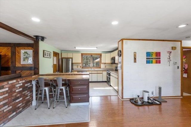 kitchen with light wood-type flooring, light countertops, a kitchen bar, stainless steel appliances, and a sink