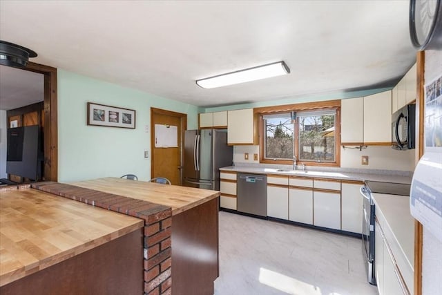 kitchen with butcher block counters, appliances with stainless steel finishes, a sink, and white cabinets