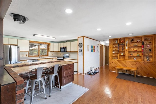 kitchen featuring a kitchen breakfast bar, light countertops, stainless steel appliances, light wood finished floors, and wooden walls
