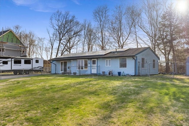 view of front facade featuring a front yard, fence, and roof mounted solar panels