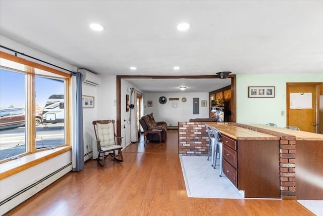kitchen featuring light wood finished floors, a healthy amount of sunlight, a baseboard heating unit, and a wall mounted air conditioner
