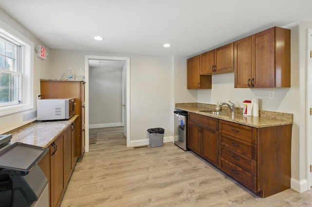 kitchen with light wood finished floors, a sink, stainless steel dishwasher, white microwave, and light stone counters