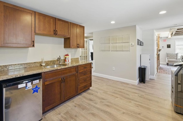 kitchen with dishwashing machine, brown cabinets, a sink, light wood-style floors, and light stone counters