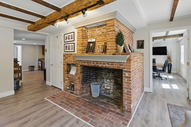 living area with wood finished floors, rail lighting, a brick fireplace, beamed ceiling, and baseboards
