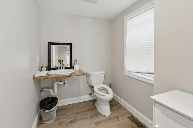 half bath featuring toilet, wood finished floors, plenty of natural light, visible vents, and baseboards