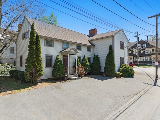 colonial home featuring a chimney and a shingled roof