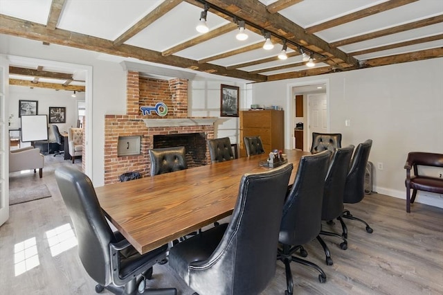 dining area with baseboards, rail lighting, a brick fireplace, wood finished floors, and beam ceiling