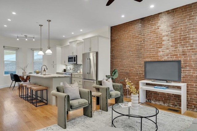 living room featuring ceiling fan, sink, light hardwood / wood-style floors, and brick wall