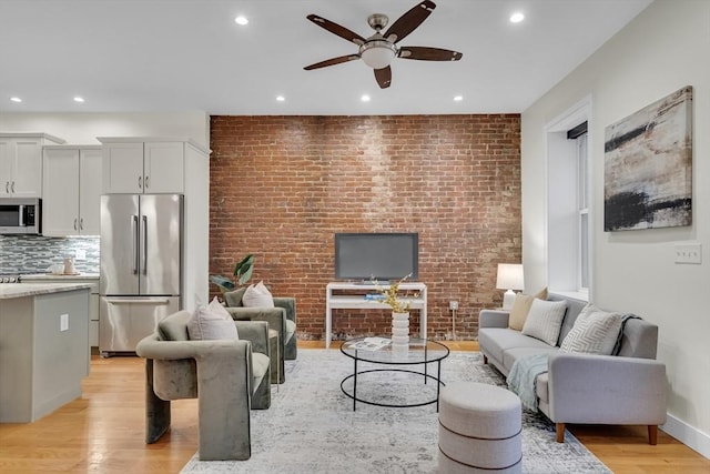 living room with ceiling fan, light hardwood / wood-style flooring, and brick wall