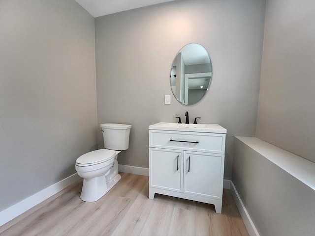 half bath with wood finished floors, toilet, baseboards, and vanity