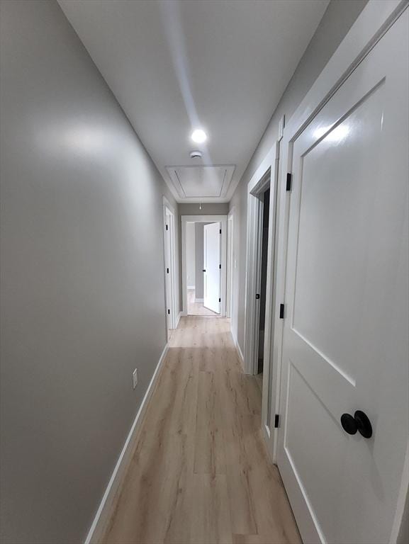 corridor with attic access, light wood-style flooring, and baseboards