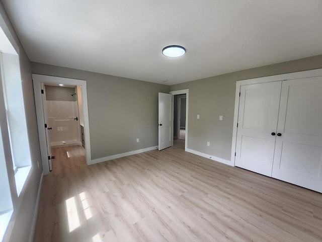 unfurnished bedroom featuring light wood finished floors, baseboards, a closet, and ensuite bath