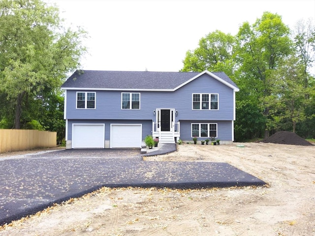 raised ranch with a garage, driveway, and fence