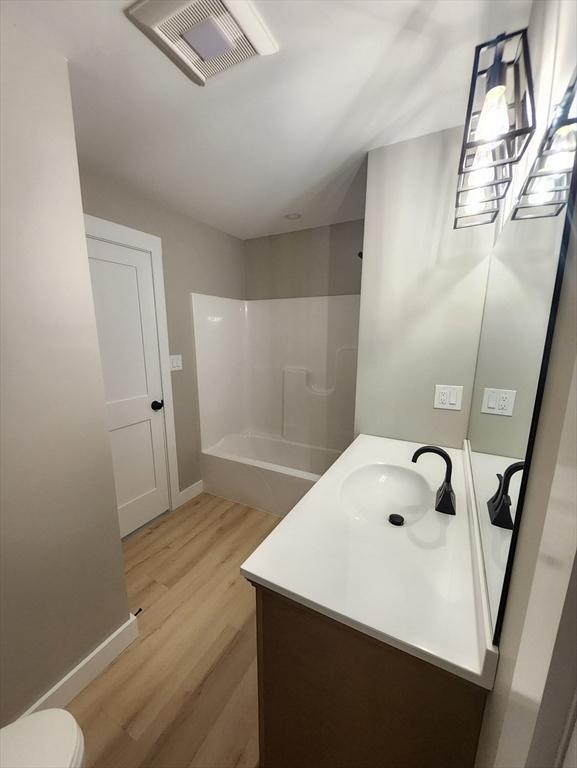 full bath with vanity, wood finished floors, baseboards, toilet, and bathtub / shower combination