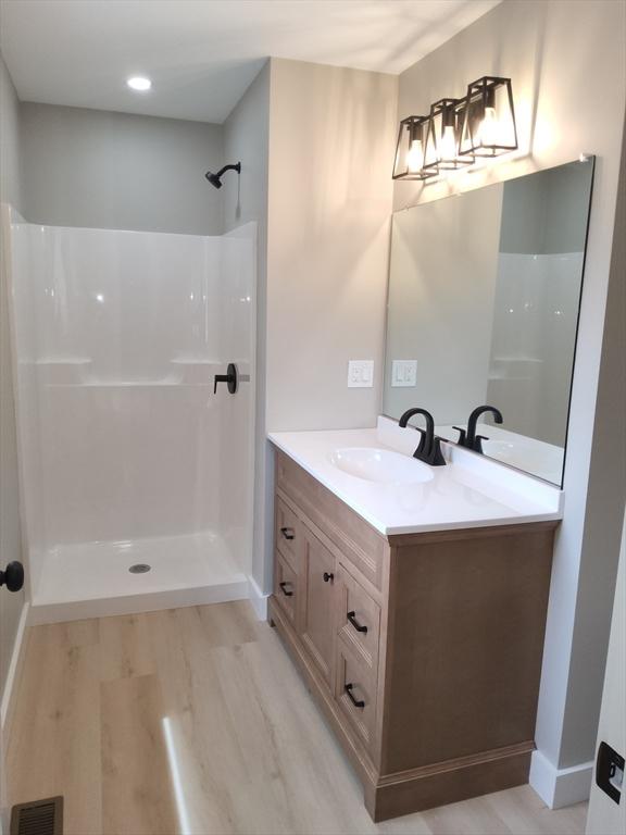 bathroom featuring vanity, a shower, wood finished floors, and baseboards