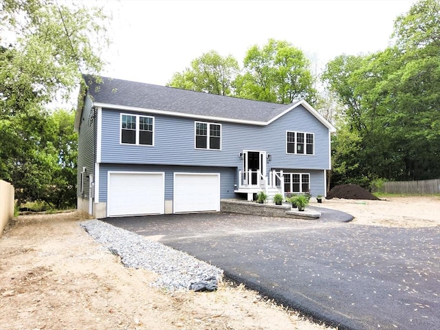split foyer home with asphalt driveway, a garage, and view of scattered trees
