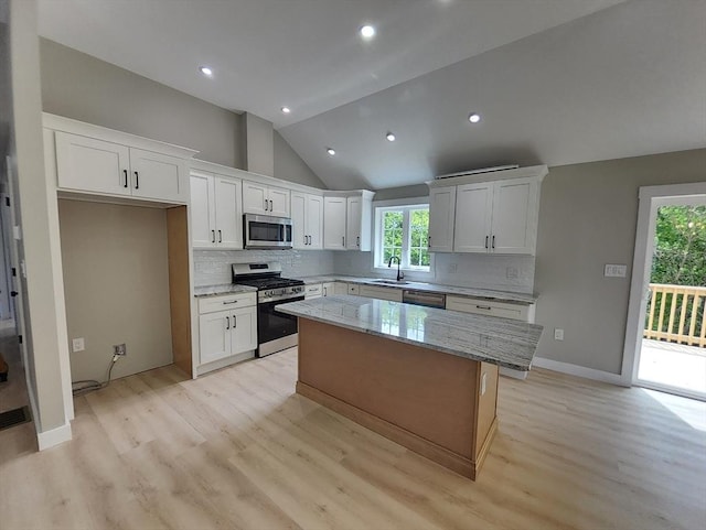 kitchen with appliances with stainless steel finishes, light wood finished floors, a sink, a kitchen island, and vaulted ceiling
