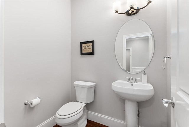 half bathroom featuring baseboards, toilet, and wood finished floors