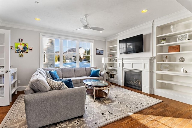 living room with built in shelves, ornamental molding, a glass covered fireplace, wood finished floors, and baseboards