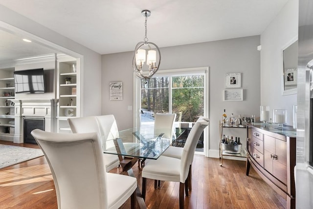 dining space featuring baseboards, a fireplace, hardwood / wood-style flooring, and a notable chandelier