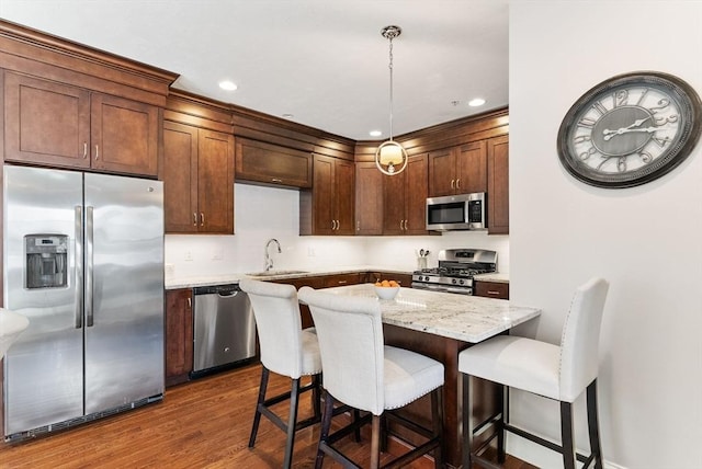 kitchen with stainless steel appliances, dark wood-style flooring, a sink, hanging light fixtures, and a kitchen bar