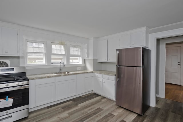 kitchen with appliances with stainless steel finishes, hardwood / wood-style floors, white cabinetry, and sink