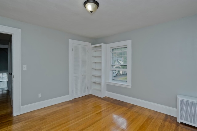 unfurnished bedroom featuring wood-type flooring, a closet, and radiator