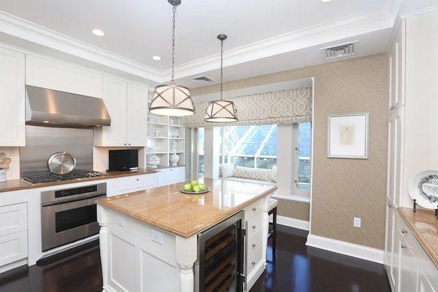 kitchen featuring tasteful backsplash, stainless steel appliances, beverage cooler, wall chimney range hood, and hanging light fixtures