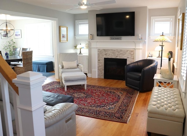 living room with a stone fireplace, ceiling fan with notable chandelier, and light wood finished floors