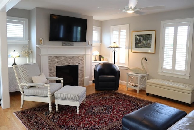 living room with light wood finished floors, a stone fireplace, baseboards, and a ceiling fan