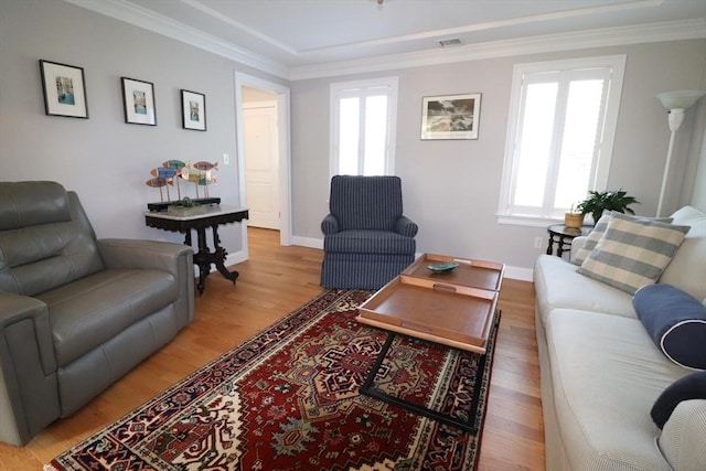 living room with visible vents, baseboards, crown molding, and light wood finished floors