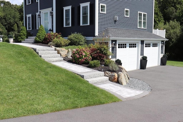 exterior space with a garage, roof with shingles, a front lawn, and aphalt driveway