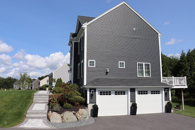 view of side of property with an attached garage, a yard, driveway, and roof with shingles