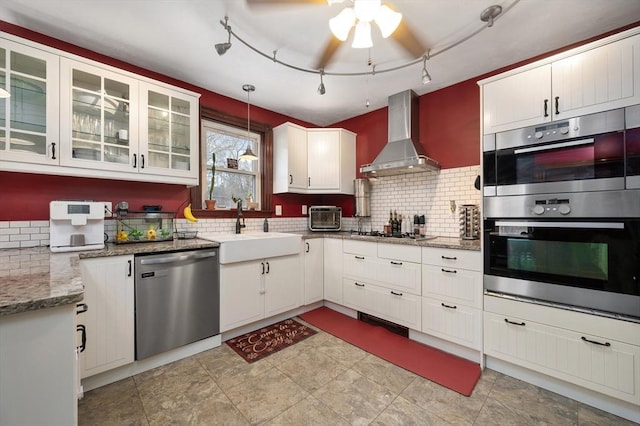 kitchen featuring stainless steel appliances, a sink, backsplash, and wall chimney exhaust hood