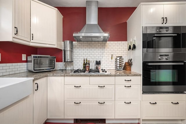 kitchen with range hood, a toaster, decorative backsplash, appliances with stainless steel finishes, and light stone countertops