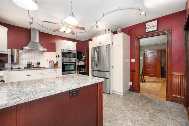 kitchen featuring white cabinets, appliances with stainless steel finishes, light stone countertops, wall chimney range hood, and backsplash