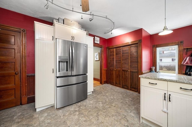 kitchen featuring stainless steel fridge, hanging light fixtures, light stone countertops, rail lighting, and white cabinetry