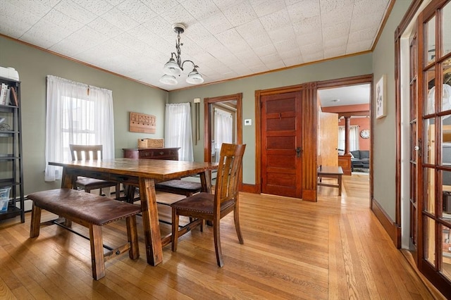 dining space featuring light wood-type flooring, baseboards, a chandelier, and crown molding