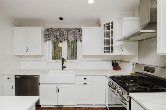 kitchen with white cabinets, a sink, decorative backsplash, wall chimney range hood, and appliances with stainless steel finishes
