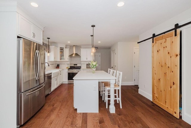 kitchen with stainless steel appliances, a barn door, white cabinetry, and wall chimney range hood