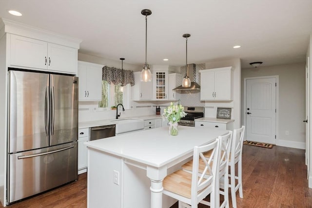 kitchen with white cabinets, stainless steel appliances, a center island, a sink, and wall chimney range hood