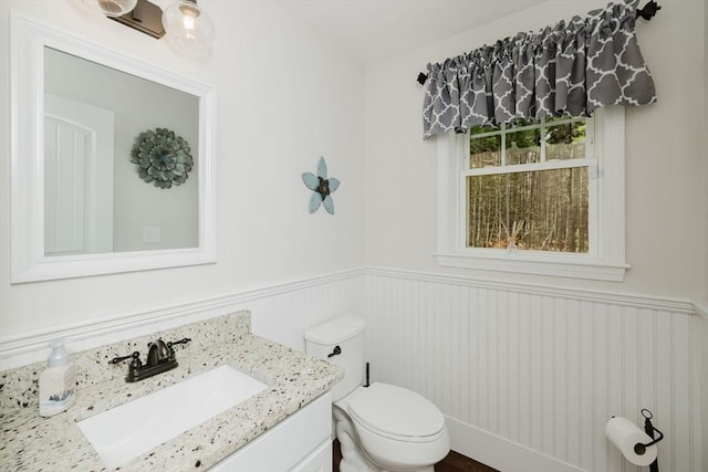 half bathroom with toilet, vanity, and wainscoting
