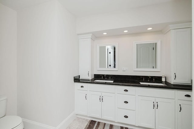 bathroom with toilet, a sink, double vanity, and recessed lighting