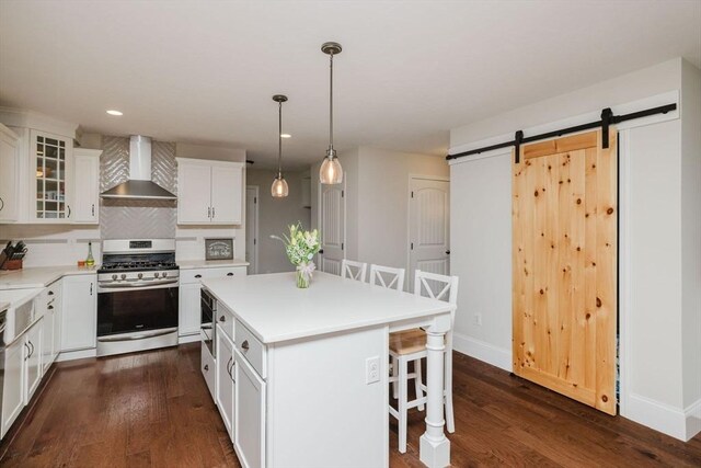 kitchen with a barn door, tasteful backsplash, wall chimney range hood, stainless steel gas stove, and a breakfast bar area