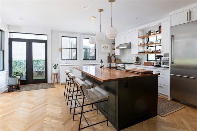 kitchen with stainless steel built in refrigerator, butcher block counters, under cabinet range hood, open shelves, and tasteful backsplash