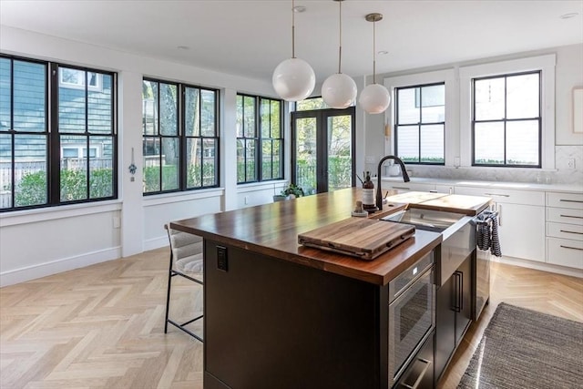 kitchen featuring wood counters, an island with sink, stainless steel microwave, pendant lighting, and white cabinets