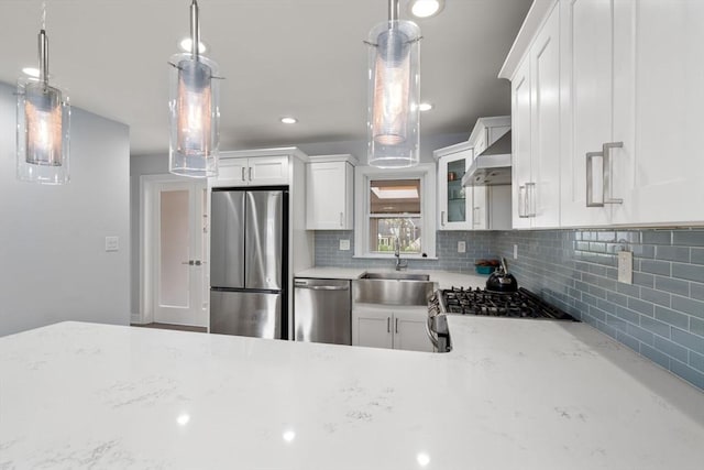 kitchen with wall chimney range hood, appliances with stainless steel finishes, a sink, and tasteful backsplash