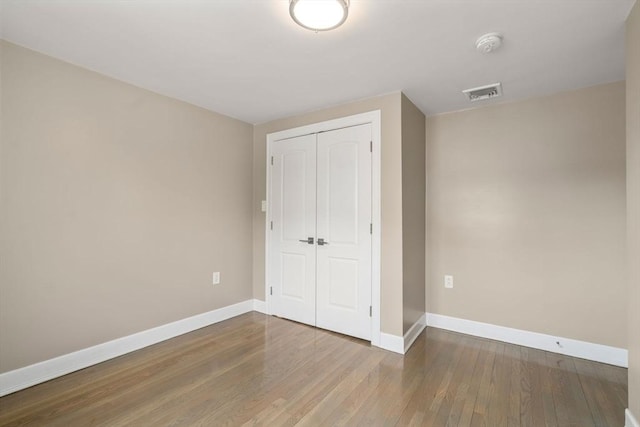 unfurnished bedroom featuring baseboards, visible vents, wood finished floors, and a closet