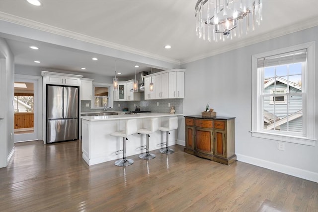kitchen with white cabinets, wall chimney range hood, freestanding refrigerator, a peninsula, and decorative backsplash