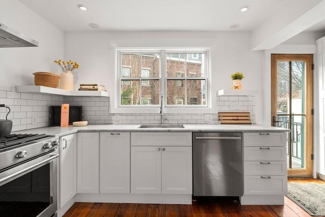 kitchen featuring plenty of natural light, wall chimney exhaust hood, appliances with stainless steel finishes, open shelves, and a sink